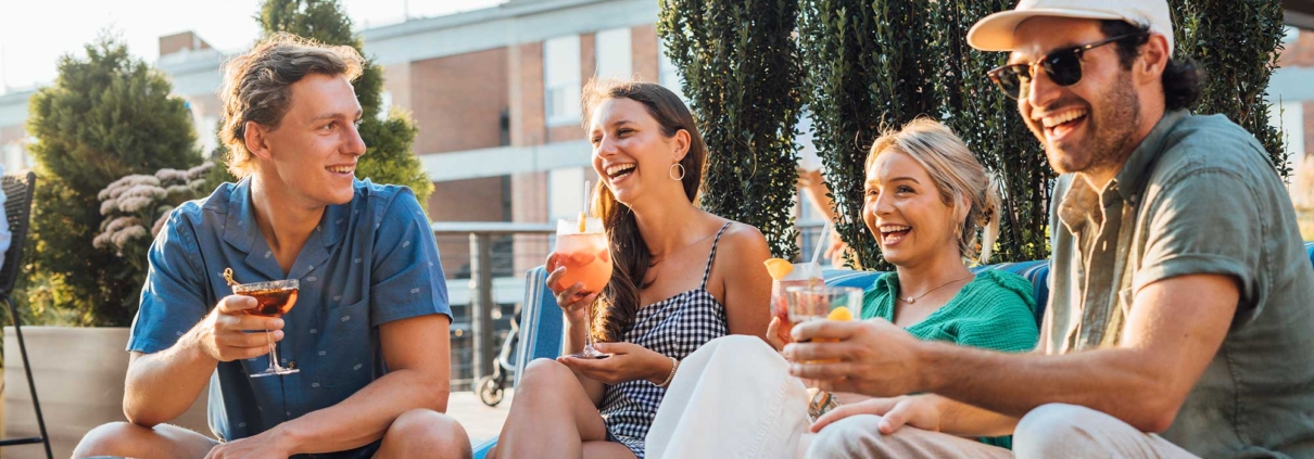Four people sitting outdoors on a patio, smiling and holding drinks while engaged in conversation, their laughter resonating with the warmth of excellent hospitality management.